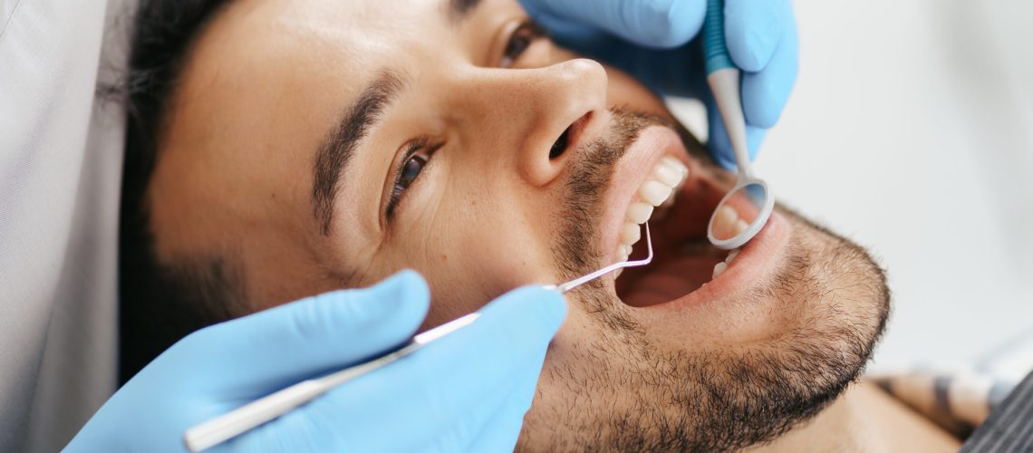 Smiling young man sitting in dentist chair while doctor examining his teeth