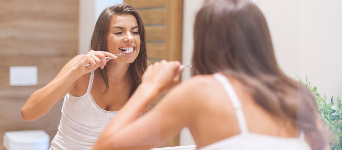 woman-brushing-teeth-in-front-of-mirror-photo-taken-through-glass